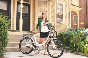 Woman with an electric bicycle in front of a suburban home, suggesting eco-friendly lifestyle and urban commuting.