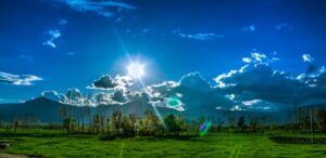 Scenic view of Kalam's green fields and dramatic sky under bright sunlight.