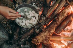 Close-up of fish being cooked over an open flame using chopsticks, outdoors.