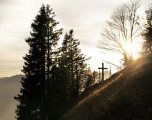 Dramatic sunset over a forest in Walenstadt, Switzerland, with a cross on a hill.