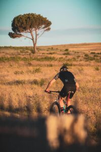A cyclist navigating a grassy landscape under the sunset, showcasing adventure and fitness.