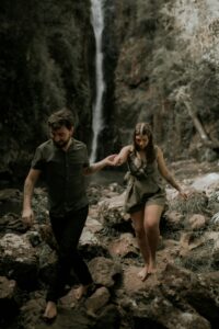 A young couple enjoys an adventurous hike near a scenic waterfall in the forest.