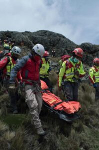 Rescue team assists injured hiker on mountainside, performing emergency aid.