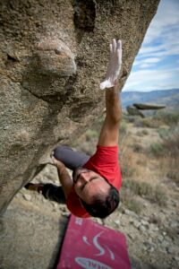 Man in red shirt bouldering on a steep rock face, showcasing strength and determination.