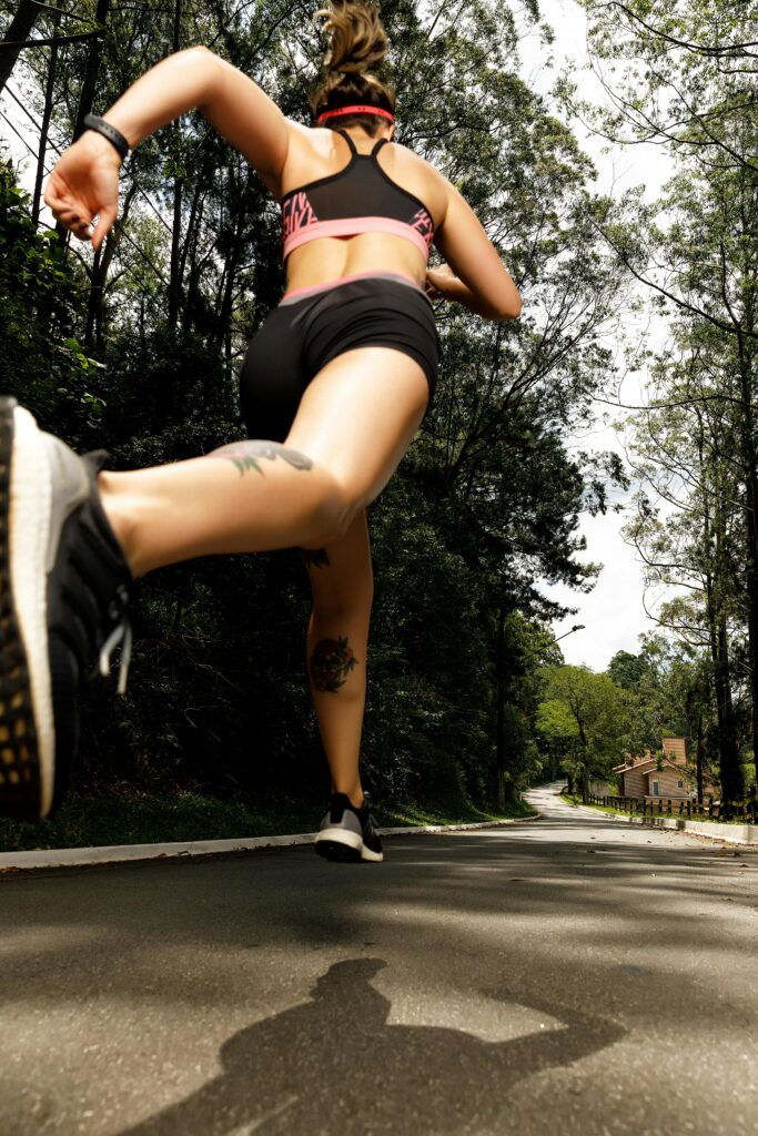 Back view of a woman in sportswear running along a tree-lined road.