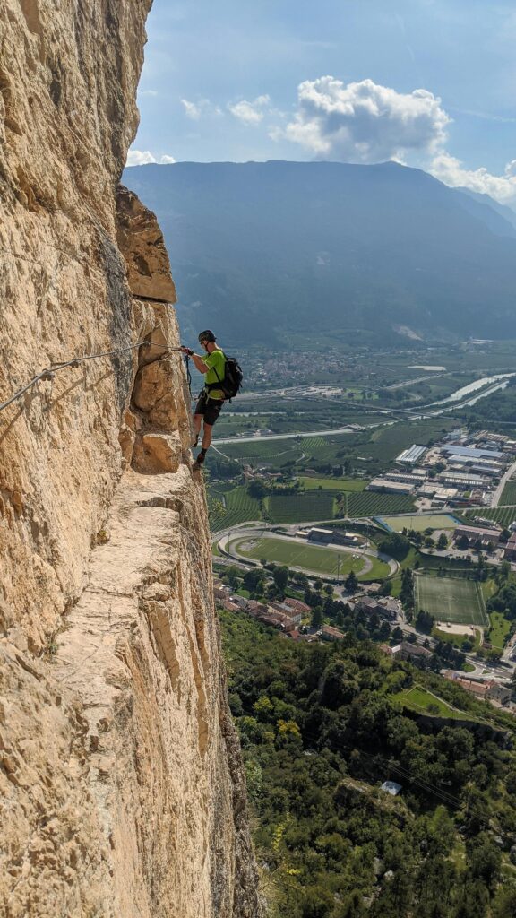 A man rock climbing the cliffs in Mori, Italy, against a breathtaking aerial view.