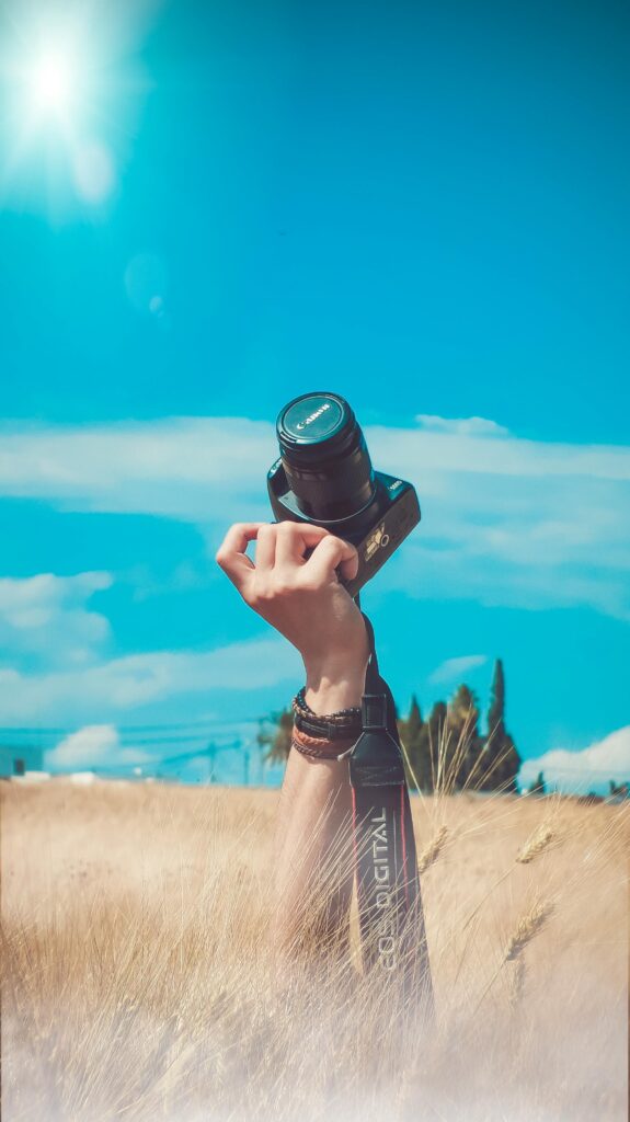 A hand raises a camera amidst a sunny field, evoking creativity and leisure.