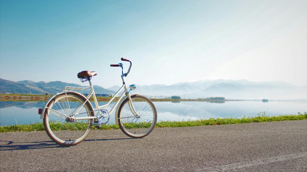 A vintage bicycle on a lakeside road with mountain views under a clear sky.