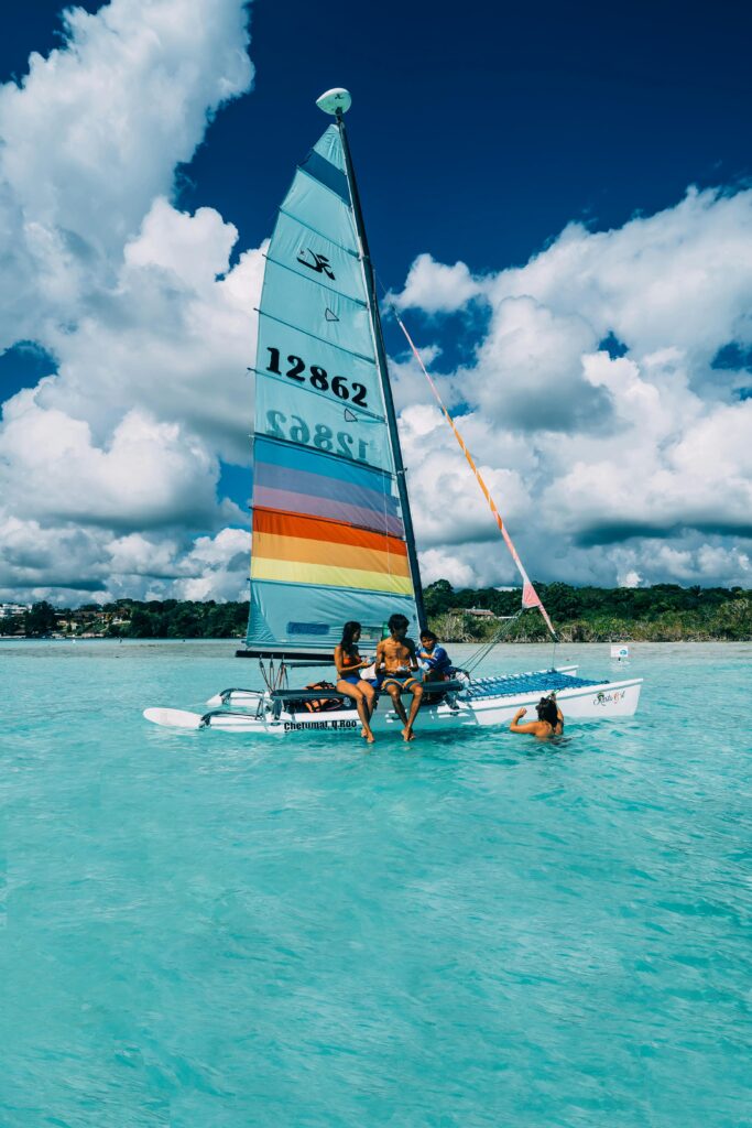 A colorful sailboat with people enjoying a sunny day in clear turquoise waters.