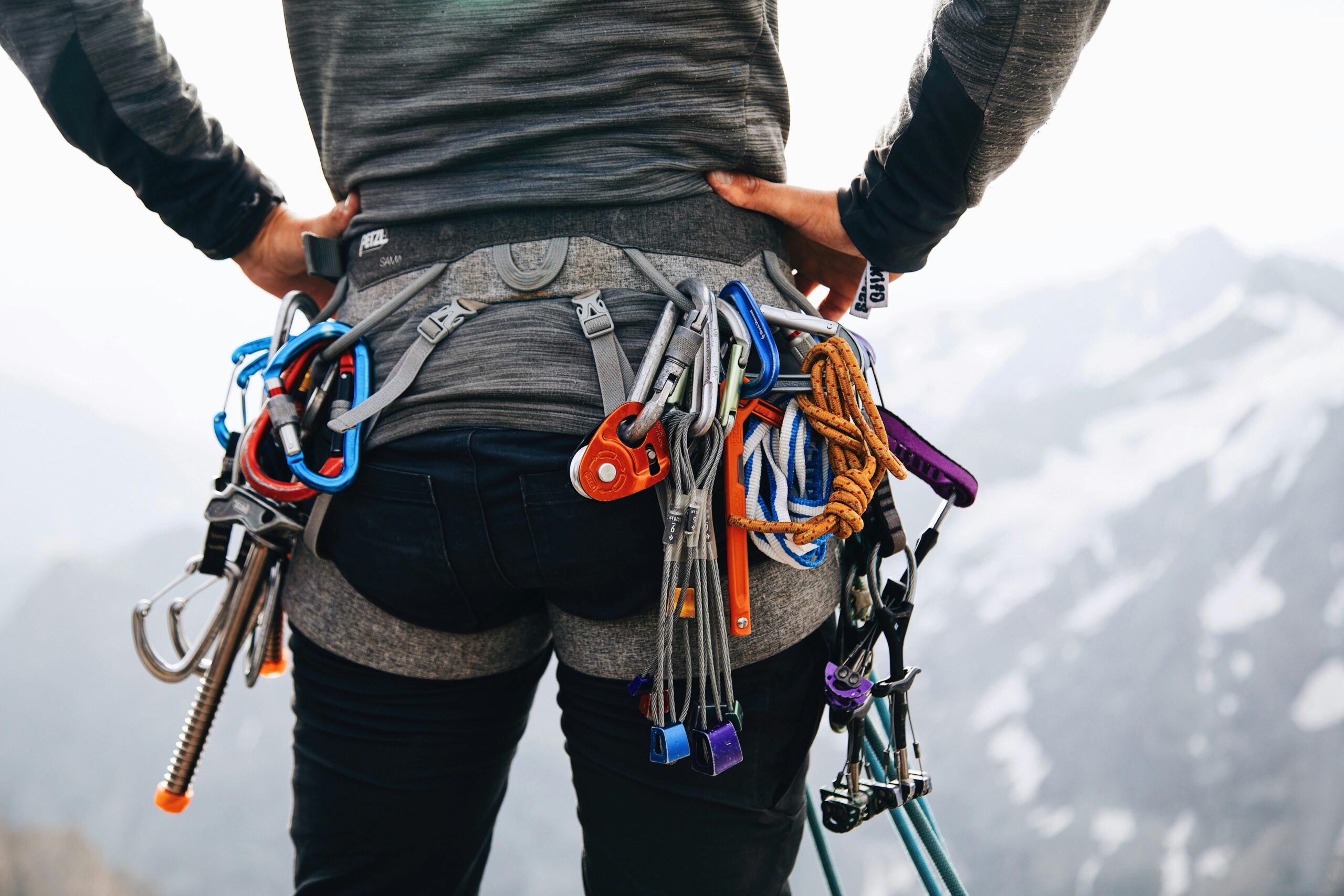 A climber stands with gear in snowy mountains, showcasing adventure and preparedness.