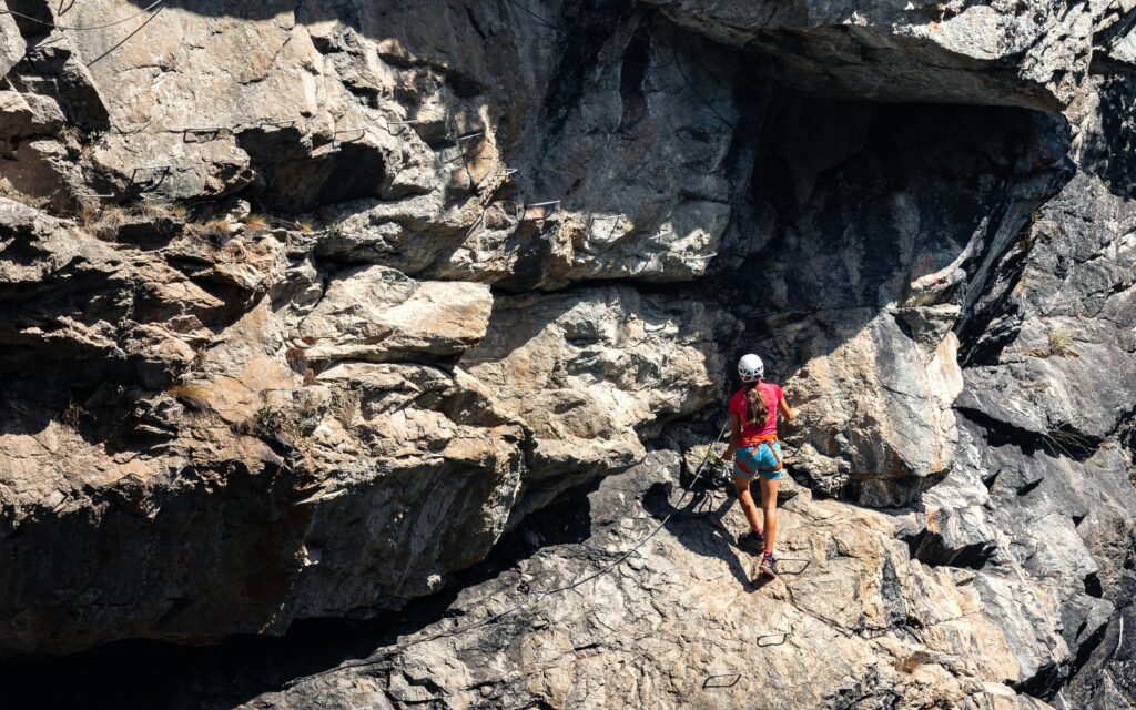 A woman skillfully climbs a rugged cliff face on a sunny summer day.