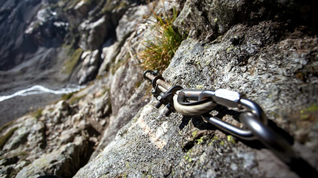 Close-up of a climbing chain anchored on a rocky mountain path, perfect for adventurous hikes.