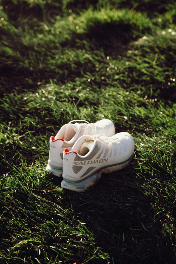 Pair of white Salomon running shoes resting on vibrant green grass under soft sunset light.