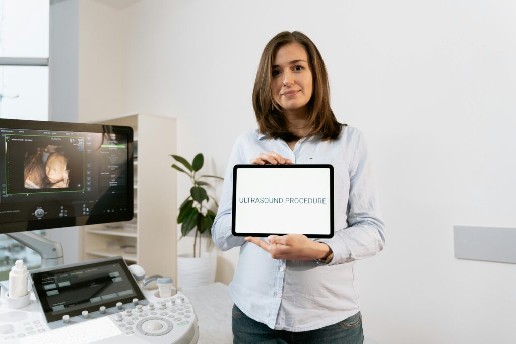 A pregnant woman holding a tablet during an ultrasound procedure in a medical clinic.